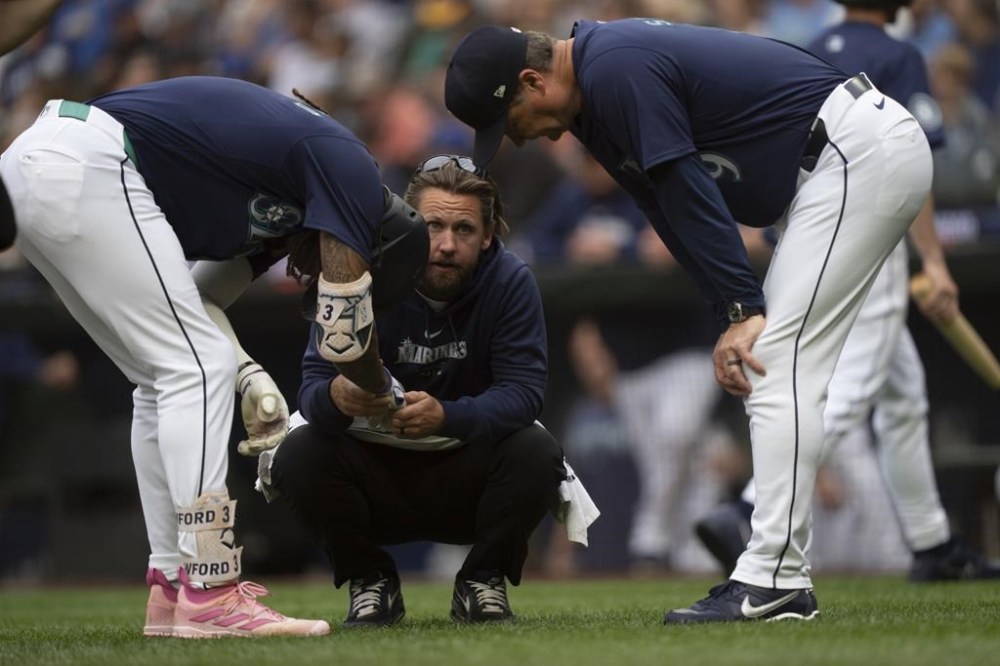 Seattle Mariners' J.P. Crawford, left, is checked by a team trainer, center, and manager Scott Servais, right, after getting hit by a pitch during the first inning of a baseball game against the Los Angeles Angels, Monday, July 22, 2024, in Seattle. (AP Photo/Stephen Brashear)