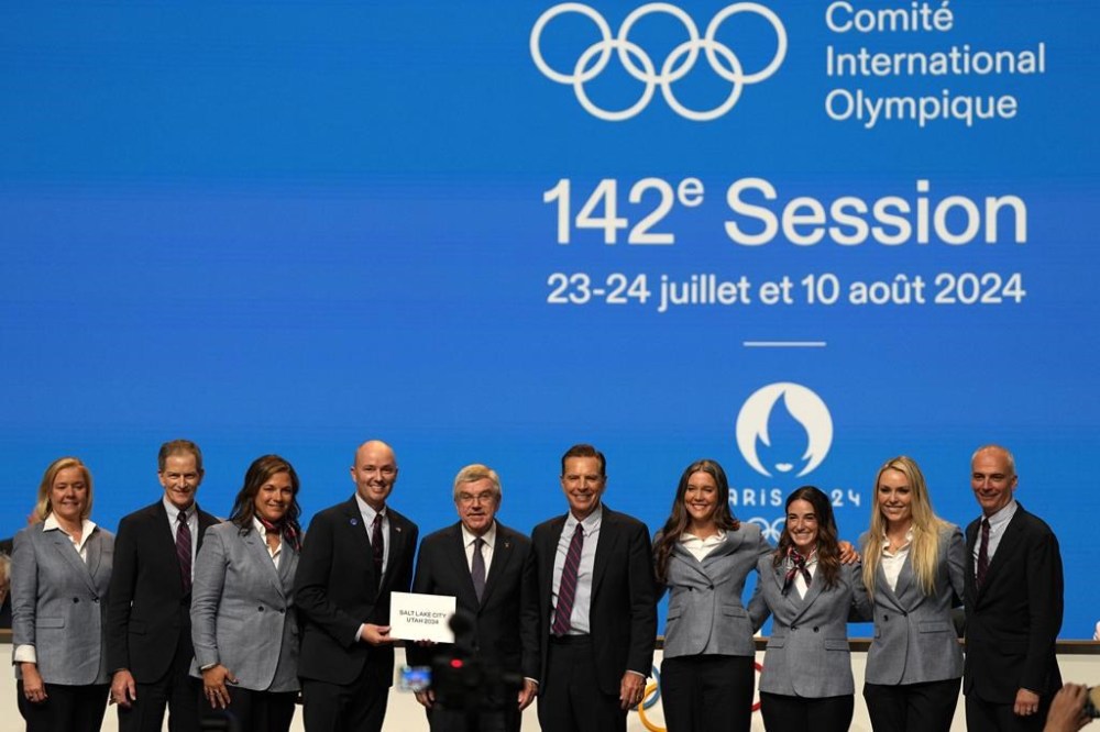 Utah Gov. Spencer Cox, fourth left, and IOC president Thomas Bach, center, pose with the Salt Lake City delegation during the 142nd IOC session at the 2024 Summer Olympics, Wednesday, July 24, 2024, in Paris, France, after Salt Lake City was confirmed as host for the 2034 Winter Games by International Olympic Committee. (AP Photo/Natacha Pisarenko)