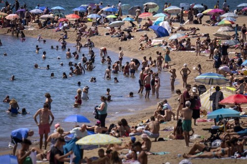 Bathers cool off in the water while others sunbathe on a Barcelona beach, Spain, Wednesday, July 24, 2024. Several regions of Spain are under alert for high temperatures. (AP Photo/Emilio Morenatti)