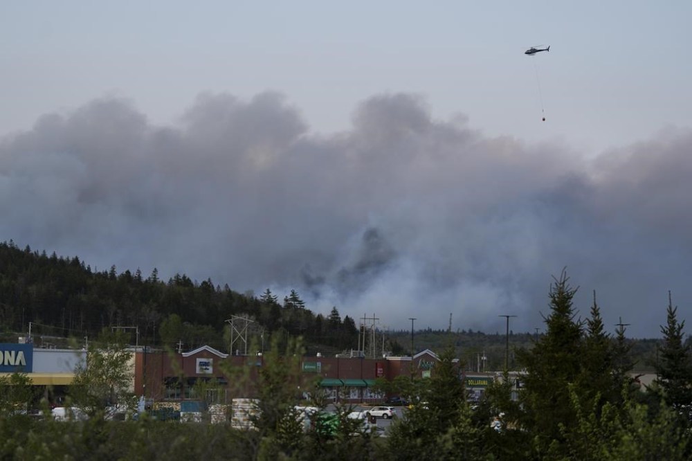 A helicopter carrying water flies over heavy smoke from an out-of-control fire in a suburban community outside Halifax that spread quickly, engulfing multiple homes and forcing the evacuation of local residents on Sunday, May 28, 2023. THE CANADIAN PRESS/Darren Calabrese