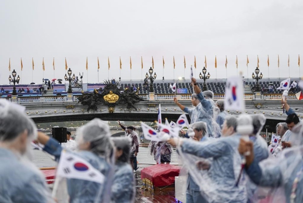 Team South Korea, wearing rain coats, wave their flag from a boat in Paris, France, during the opening ceremony of the 2024 Summer Olympics, Friday, July 26, 2024. (AP Photo/Lee Jin-man, Pool)