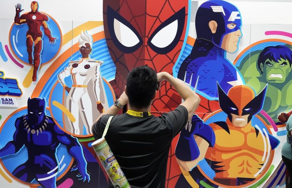 An attendee takes a picture of an illustrated wall of Marvel superhero characters during preview night for Comic-Con International, Wednesday, July 24, 2024, in San Diego. (AP Photo/Chris Pizzello)