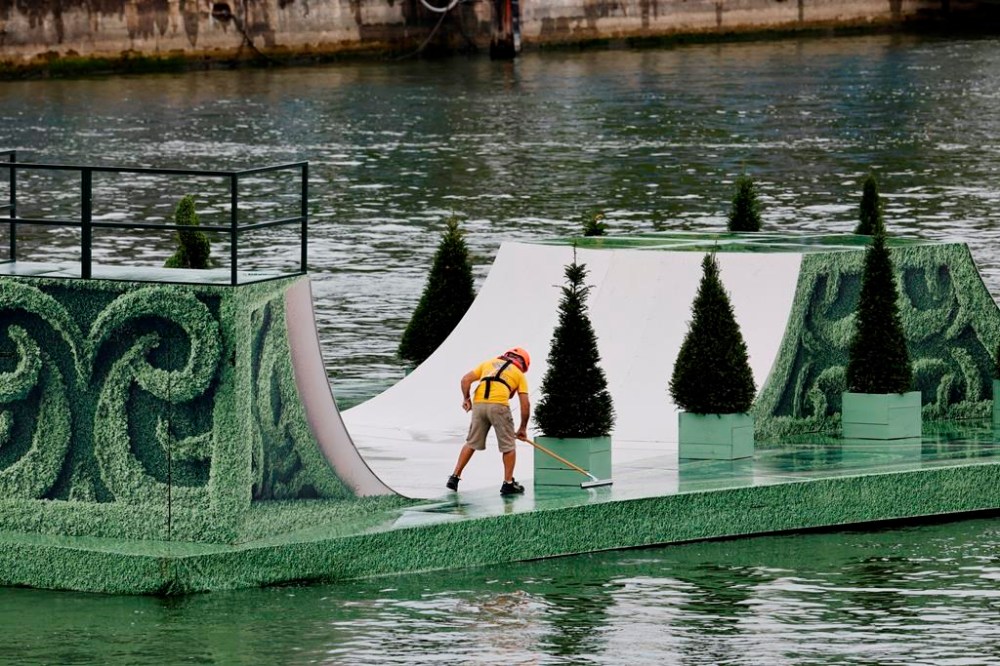 A maintenance worker sweeps water off a skateboard ramp installed on a floating platform ahead of the opening ceremony for the 2024 Summer Olympics in Paris, France, Friday, July 26, 2024. (Stefan Wermuth/Pool Photo via AP)
