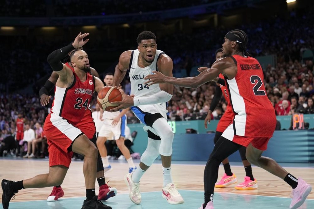 Giannis Antetokounmpo, of Greece, drives between Dillon Brooks, left, and Shai Gilgeous-Alexander, of Canada, in a men's basketball game at the 2024 Summer Olympics, Saturday, July 27, 2024 in Villeneuve-d'Ascq, France. (AP Photo/Mark J. Terrill)