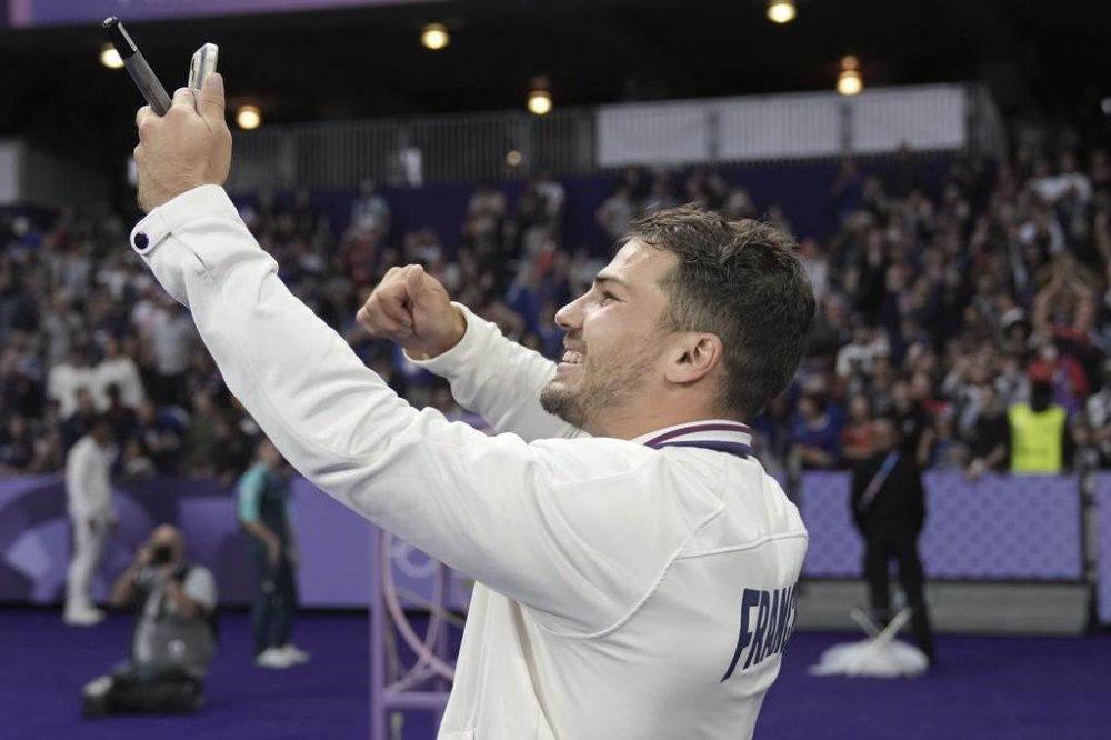 Antoine Dupont of France holds up his gold medal as he looks at his mobile phone as he celebrates after France won the men's Rugby Sevens gold medal at the 2024 Summer Olympics, in the Stade de France, in Saint-Denis, France, Saturday, July 27, 2024. France defeated Fiji in the gold medal match 28-7. (AP Photo/Tsvangirayi Mukwazhi)