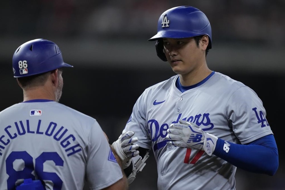 Los Angeles Dodgers designated hitter Shohei Ohtani, right, is congratulated by first base coach Clayton McCullough, left, after hitting an RBI single during the sixth inning of a baseball game against the Houston Astros, Saturday, July 27, 2024, in Houston. (AP Photo/Kevin M. Cox)