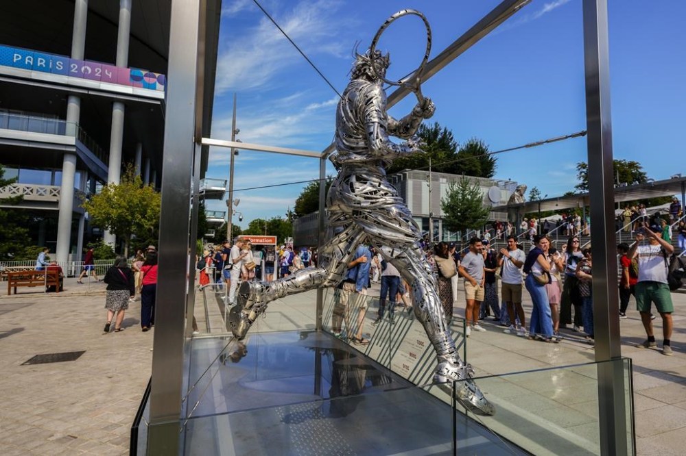 People gather next to the statue of Spanish artist Jordi Diez representing Spain's Rafael Nadal at the Roland Garros stadium during the 2024 Summer Olympics, Sunday, July 28, 2024, in Paris, France. (AP Photo/Manu Fernandez)