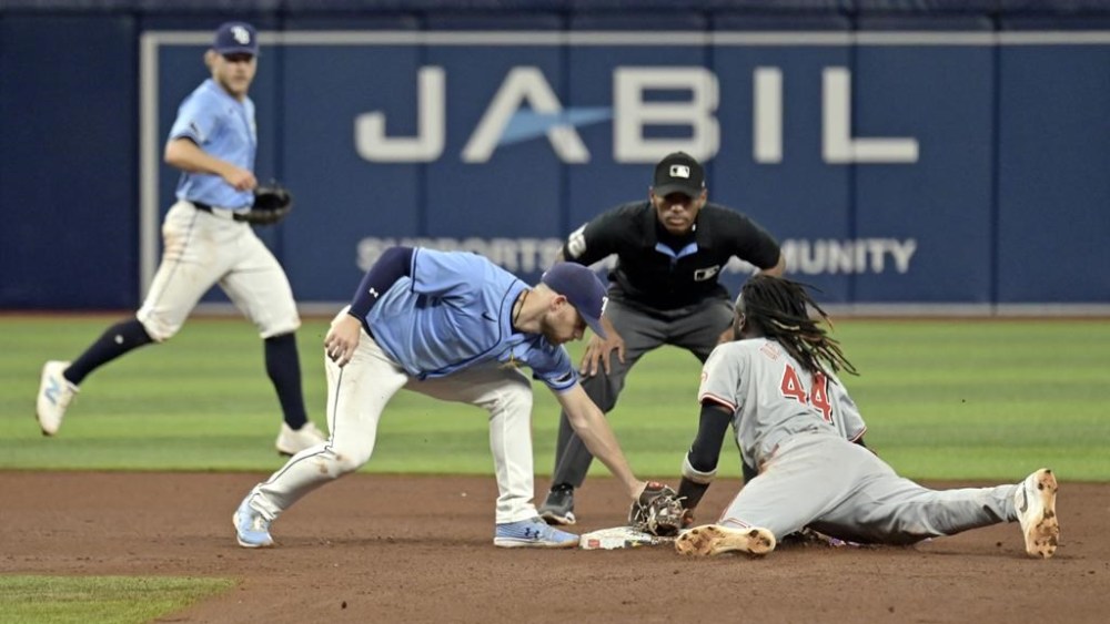 Tampa Bay Rays shortstop Taylor Walls, left, and umpire Edwin Moscoso, center, watch as Cincinnati Reds' Elly De La Cruz (44) bats the tag from Brandon Lowe for a stolen base during the sixth inning of a baseball game, Sunday, July 28, 2024, in St. Petersburg, Fla. (AP Photo/Steve Nesius)