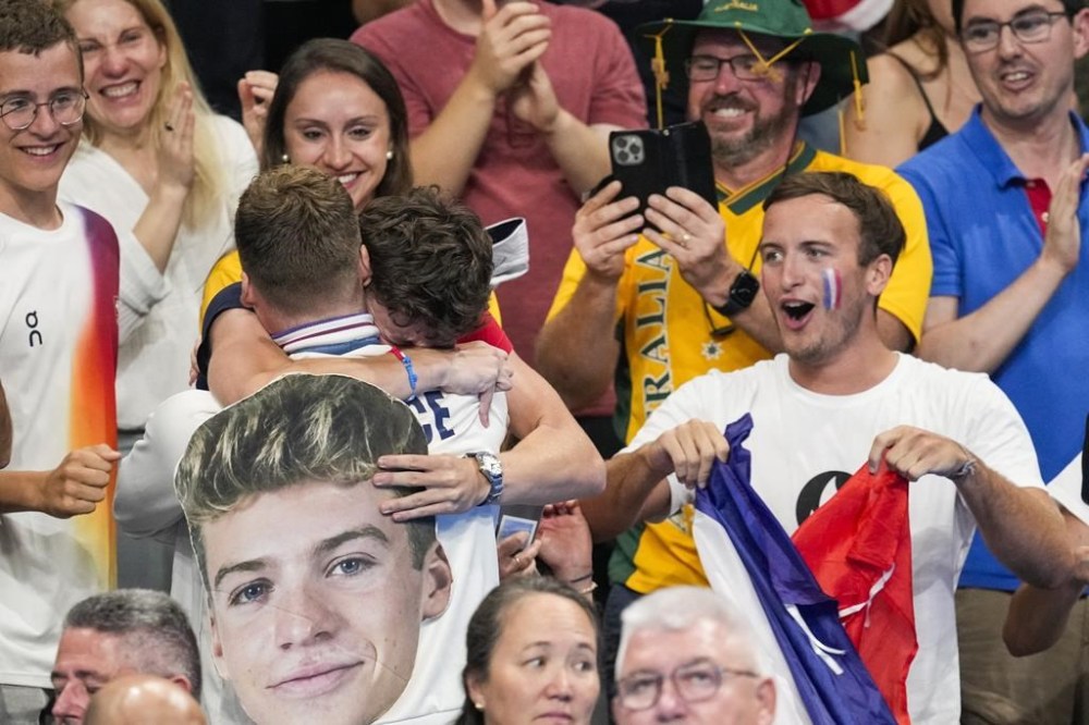 Gold medalist, Leon Marchand, left, of France, greets a fan after the men's 400-meter individual medley final at the 2024 Summer Olympics, Sunday, July 28, 2024, in Nanterre, France. (AP Photo/Bernat Armangue)