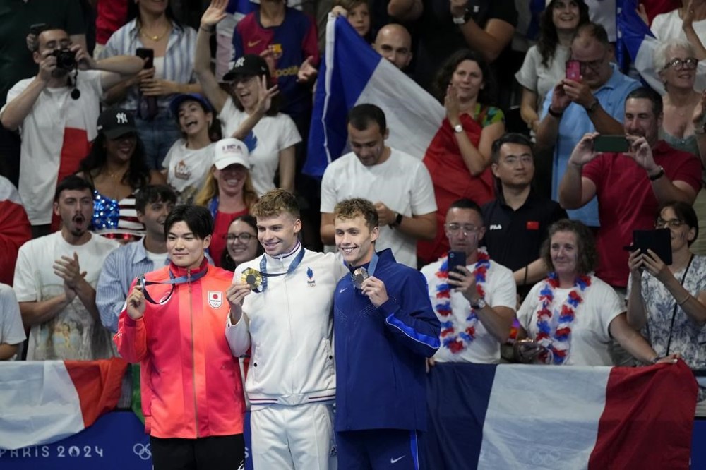Gold medalist Leon Marchand, foreground center, of France, stands with silver medalist Tomoyuki Matsushita, foregound left, of Japan, and bronze medalist Carson Foster, of the United States, following the men's 400-meter individual medley final at the 2024 Summer Olympics, Sunday, July 28, 2024, in Nanterre, France.(AP Photo/Petr David Josek)
