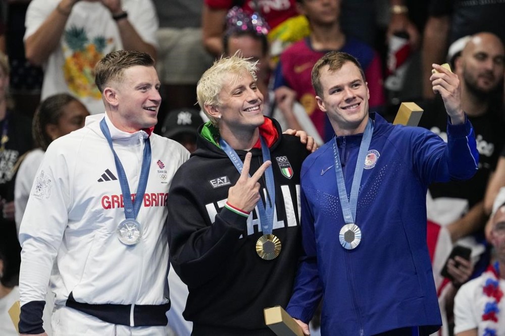 Gold medalist, Nicolo Martinenghi, center, of Italy, stands with silver medalists, Nic Fink, right, of the the United States, and Adam Peaty, of Britain, on the podium after the men's 100-meter breaststroke final at the 2024 Summer Olympics, Sunday, July 28, 2024, in Nanterre, France. (AP Photo/Bernat Armangue)