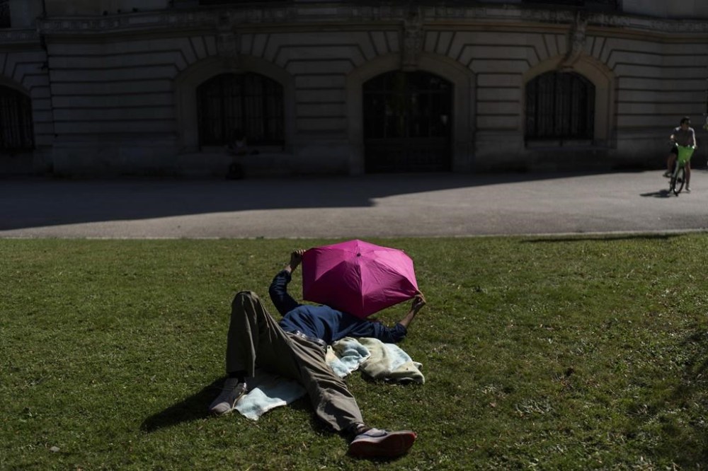 A man uses an umbrella to shield himself from the hot afternoon sun near the Grand Palais fencing venue at the 2024 Summer Olympics, Monday, July 29, 2024, in Paris. (AP Photo/David Goldman)