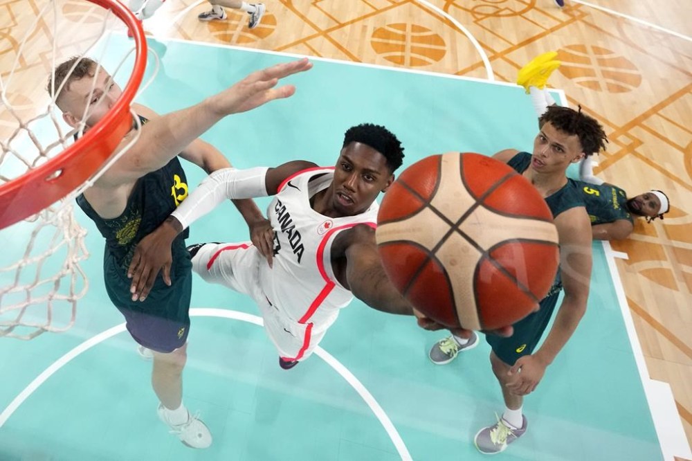 Canada's RJ Barrett, center, shoots as Australia's Jock Landale, left, and Australia's Dyson Daniels defend during a men's basketball game at the 2024 Summer Olympics, Tuesday, July 30, 2024, in Villeneuve-d'Ascq, France. (AP Photo/Michael Conroy, Pool)