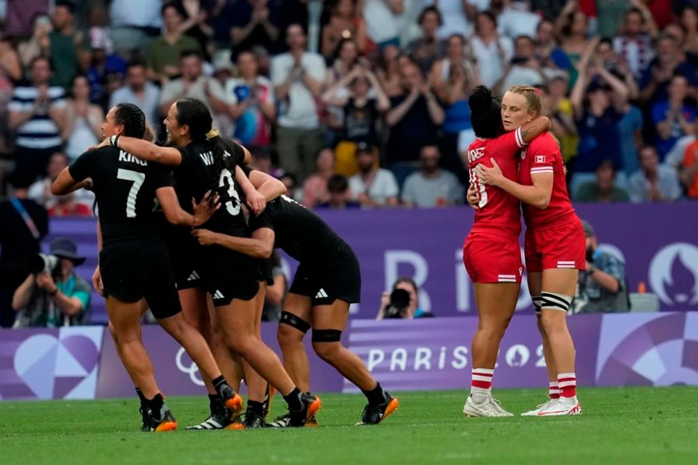 New Zealand players celebrate their win as Canada back Fancy Bermudez (10) hugs teammate Carissa Norsten (right) following the women's rugby sevens gold medal match at the Summer Olympics in Paris on Tuesday, July 30, 2024. THE CANADIAN PRESS/Adrian Wyld