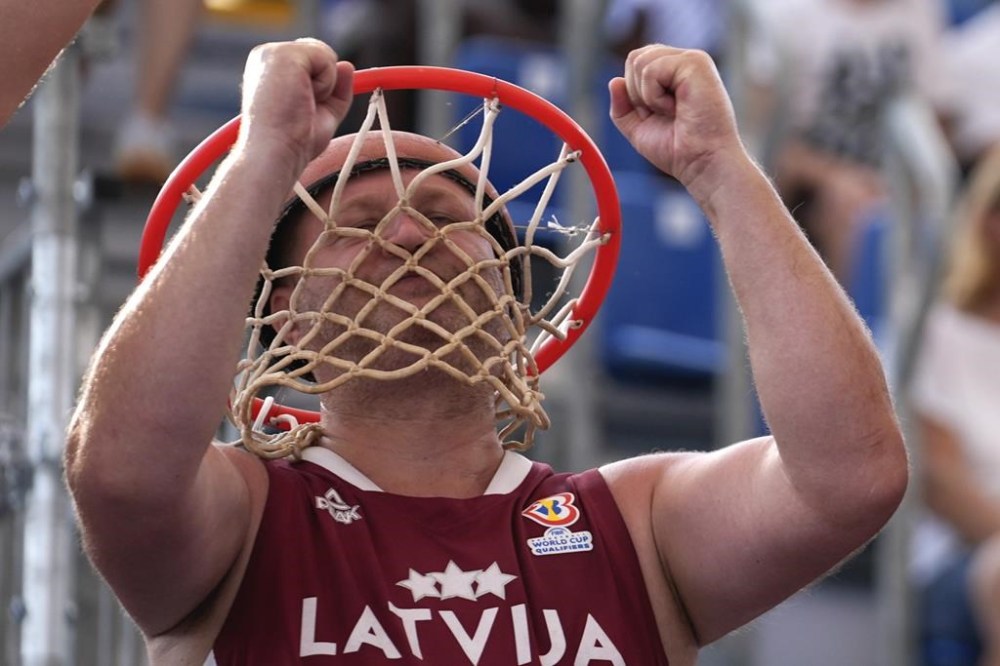 A Latvia fan wearing a basketball net on his head cheers during the men's 3x3 basketball pool round match between Latvia and Lithuania at the 2024 Summer Olympics, Tuesday, July 30, 2024, in Paris, France. (AP Photo/Rebecca Blackwell)