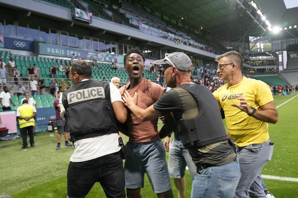 Security guards grab a pitch invader during the men's Group A soccer match between the United States and Guinea at Geoffroy-Guichard Stadium during the 2024 Summer Olympics, Tuesday, July 30, 2024, in Saint-Etienne, France. (AP Photo/Silvia Izquierdo)
