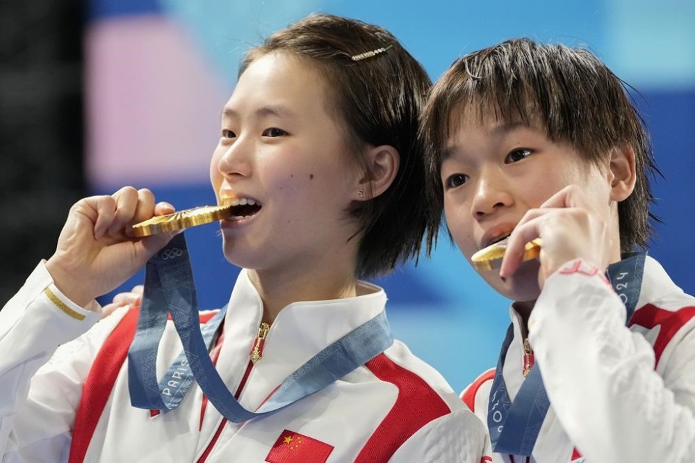 China's Chen Yuxi and Quan Hongchan bite their gold medal on the podium of the women's synchronised 10m platform diving final at the 2024 Summer Olympics, Wednesday, July 31, 2024, in Saint-Denis, France. (AP Photo/Jin Lee Man)