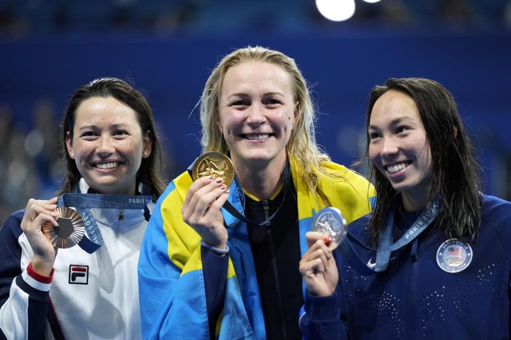 Gold medalist Sarah Sjoestroem, of Sweden, stands with silver medalist Torri Huske, of the United States, right, and bronze medalist Siobhan Bernadette Haughey, of Hong Kong, on the podium after the women's 100-meter freestyle final at the 2024 Summer Olympics, Wednesday, July 31, 2024, in Nanterre, France. (AP Photo/Ashley Landis)