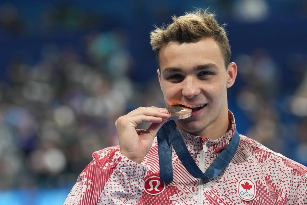 Ilya Kharun, of Canada, bites down on his bronze medal after competing in the men's 200-metre butterfly final at the 2024 Summer Olympics in Nanterre, France on Wednesday, July 31, 2024. THE CANADIAN PRESS/Nathan Denette