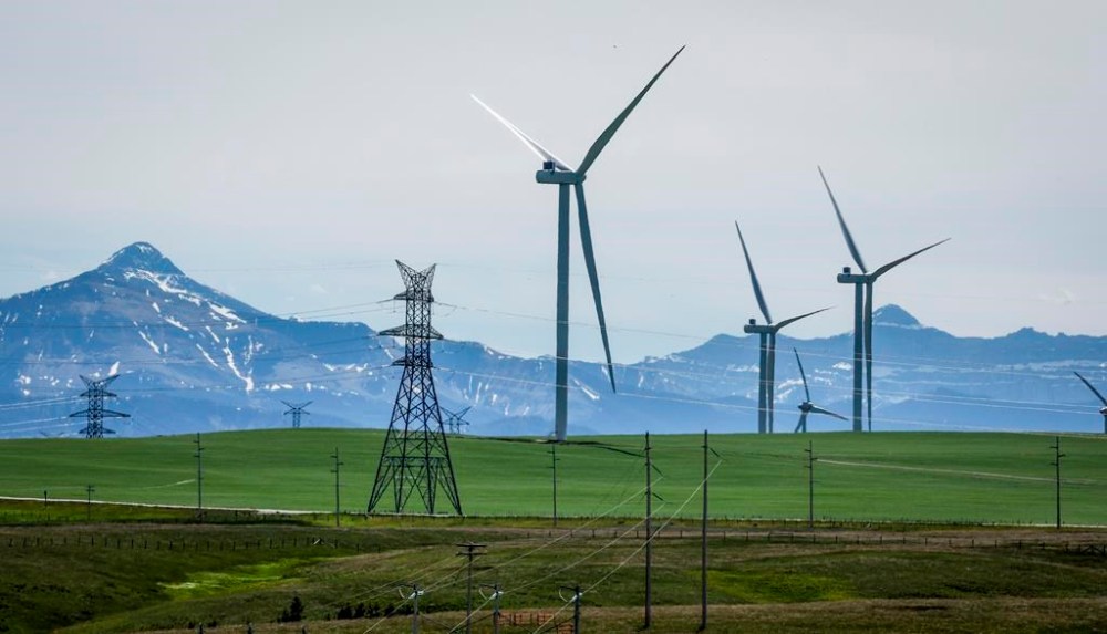 An analysis suggests that a year after Alberta imposed a seven-month moratorium on renewable power approvals, there have been dozens of cancelled projects and legal uncertainty. Power transmission lines and wind turbines as seen with the Rocky Mountains in the background near Pincher Creek, Alta., Thursday, June 6, 2024. THE CANADIAN PRESS/Jeff McIntosh