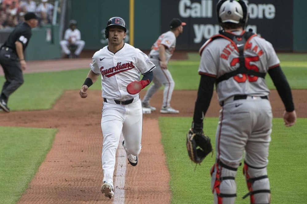 Cleveland Guardians' Steven Kwan, front left, scores on a sacrifice fly by Jose Ramirez as Baltimore Orioles' Adley Rutschman, right, stands by during the first inning of a baseball game in Cleveland, Thursday, Aug. 1, 2024. (AP Photo/Phil Long)