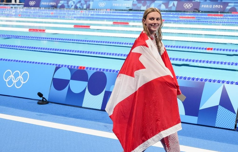 Canada's Summer McIntosh, of Toronto, wears the flag as she celebrates her win and new Olympic record in the 200m women's butterfly final during the 2024 Summer Olympic Games, in Paris, France, Thursday, Aug. 1, 2024. THE CANADIAN PRESS/Christinne Muschi
