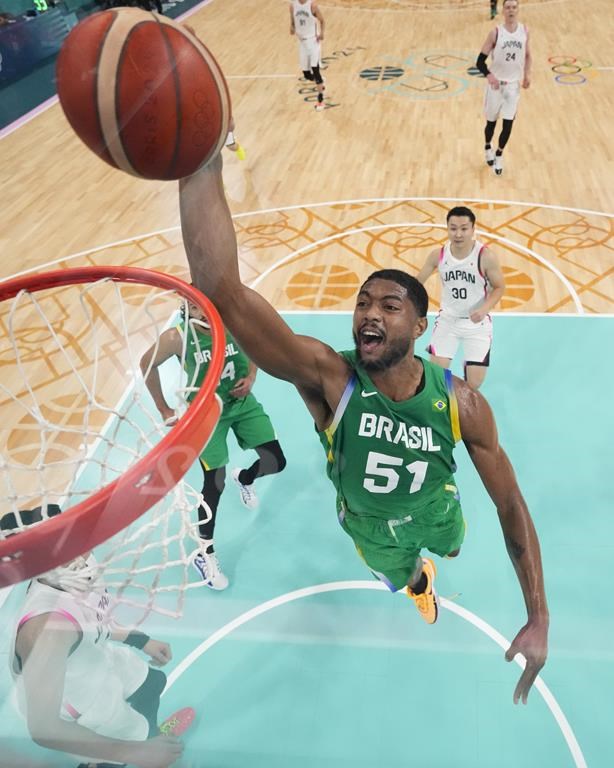 Bruno Caboclo, of Brazil, gets a basket on a dunk in front of Keisei Tominaga, of Japan, in a men's basketball game at the 2024 Summer Olympics, Friday, Aug. 2, 2024, in Villeneuve-d'Ascq, France. (AP Photo/Mark J. Terrill, Pool)