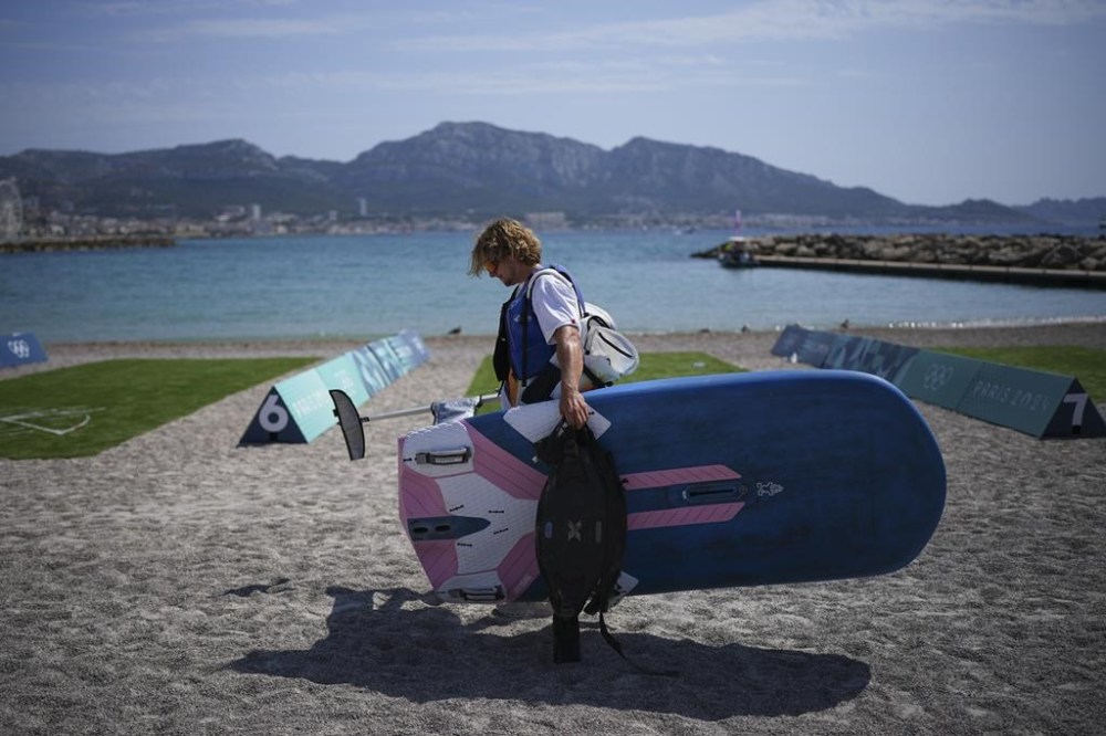 Elia Colombo of Switzerland carries his windsurf board after the men's windsurfing medal race was postponed until Saturday due to lack of wind during the 2024 Summer Olympics, Friday, Aug. 2, 2024, in Marseille, France. (AP Photo/Daniel Cole)
