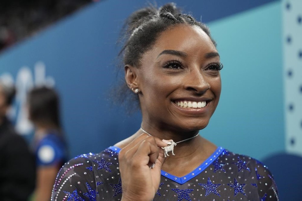 Simone Biles, of the United States, celebrates with her GOAT necklace after winning the gold medal during the women's artistic gymnastics all-around finals in Bercy Arena at the 2024 Summer Olympics, Thursday, Aug. 1, 2024, in Paris, France. (AP Photo/Charlie Riedel)