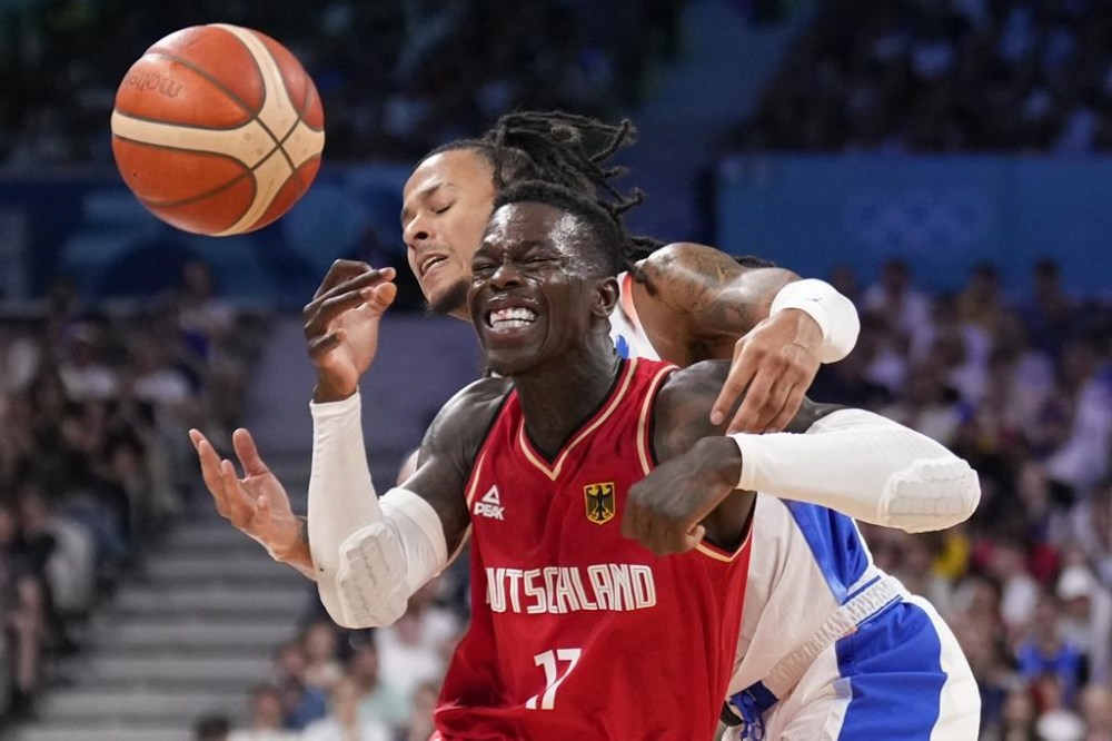 Dennis Schroder, of Germany, is hit as he drives past Matthew Strazel, of France, in a men's basketball game at the 2024 Summer Olympics, Friday, Aug. 2, 2024, in Villeneuve-d'Ascq, France. (AP Photo/Mark J. Terrill)