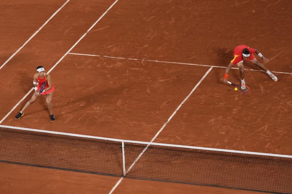 China's Zhang Zhizhen returns the ball as Wang Xinyu looks on as they play Czech Republic's Tomas Machac and Katerina Siniakova during the Mixed Doubles final tennis match at the Roland Garros stadium at the 2024 Summer Olympics, Friday, Aug. 2, 2024, in Paris, France. (AP Photo/Manu Fernandez)