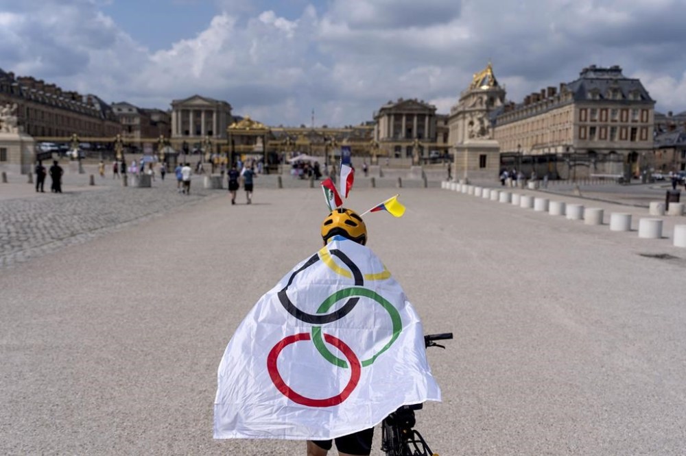 Gonzalo Dominguez, of Mexico City, wears an Olympic flag as he tours the grounds of the Chateau de Versailles, site of the equestrian events during the 2024 Summer Olympics, Friday, Aug. 2, 2024, in Versailles, France. Once the residence of French royalty, the chateau is one of the most popular tourist spots in Paris. Under the monarchy, horses were used by the royal family, its entourage and visitors to go hunting, show their equestrian skills and enjoy rides in the Versailles gardens. They were an essential part of festivities and a symbol of the king's power. (AP Photo/David Goldman)