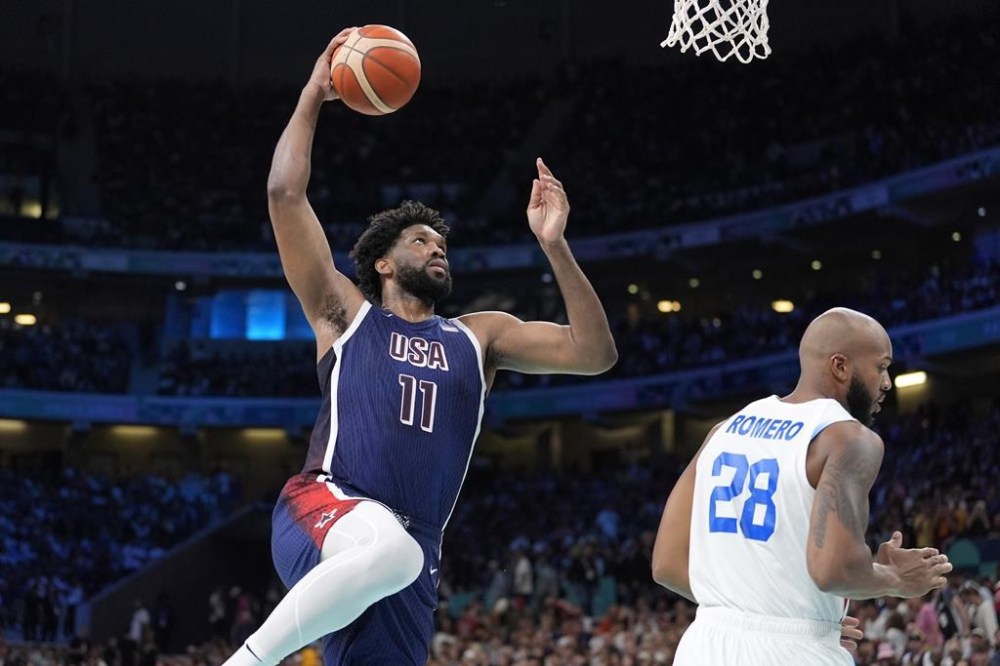 United States' Joel Embiid, left, goes up for a dunk as Puerto Rico's Ismael Romero defends during a men's basketball game at the 2024 Summer Olympics, Saturday, Aug. 3, 2024, in Villeneuve-d'Ascq, France. (AP Photo/Michael Conroy)