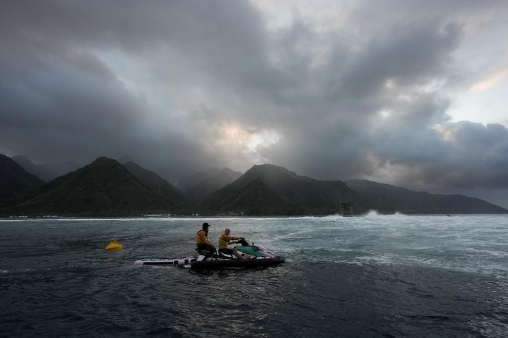 Members of the water safety team look on from a jet ski as the sun rises on a training day ahead of the 2024 Summer Olympics surfing competition, Tuesday, July 23, 2024, in Teahupo'o, Tahiti. (AP Photo/Gregory Bull)
