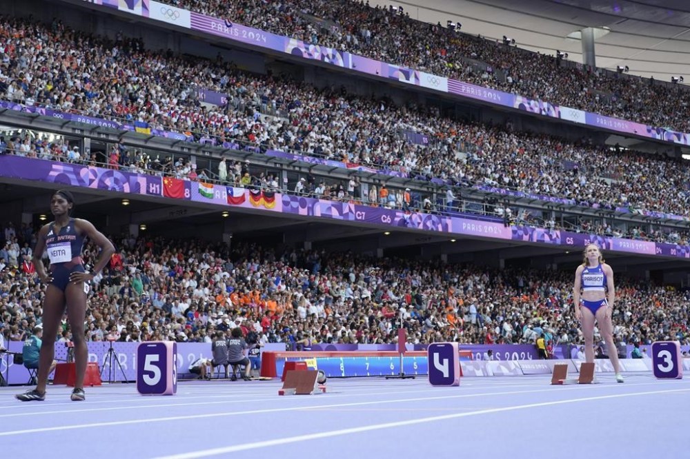 Helene Parisot, right, of France, and Daryll Neita, left, of Britain, stand near the empty start blocks for Shericka Jackson, of Jamaica, ahead of their women's 200-meter heat at the 2024 Summer Olympics, Sunday, Aug. 4, 2024, in Saint-Denis, France. (AP Photo/Bernat Armangue)