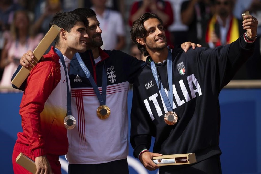 Serbia's Novak Djokovic, center, gold medalist, Spain's Carlos Alcaraz, left, silver medalist, and Italian bronze medalist Lorenzo Musetti take a selfie on the podium after the men's singles tennis final at the Roland Garros stadium during the 2024 Summer Olympics, Sunday, Aug. 4, 2024, in Paris, France. (AP Photo/Louise Delmotte)