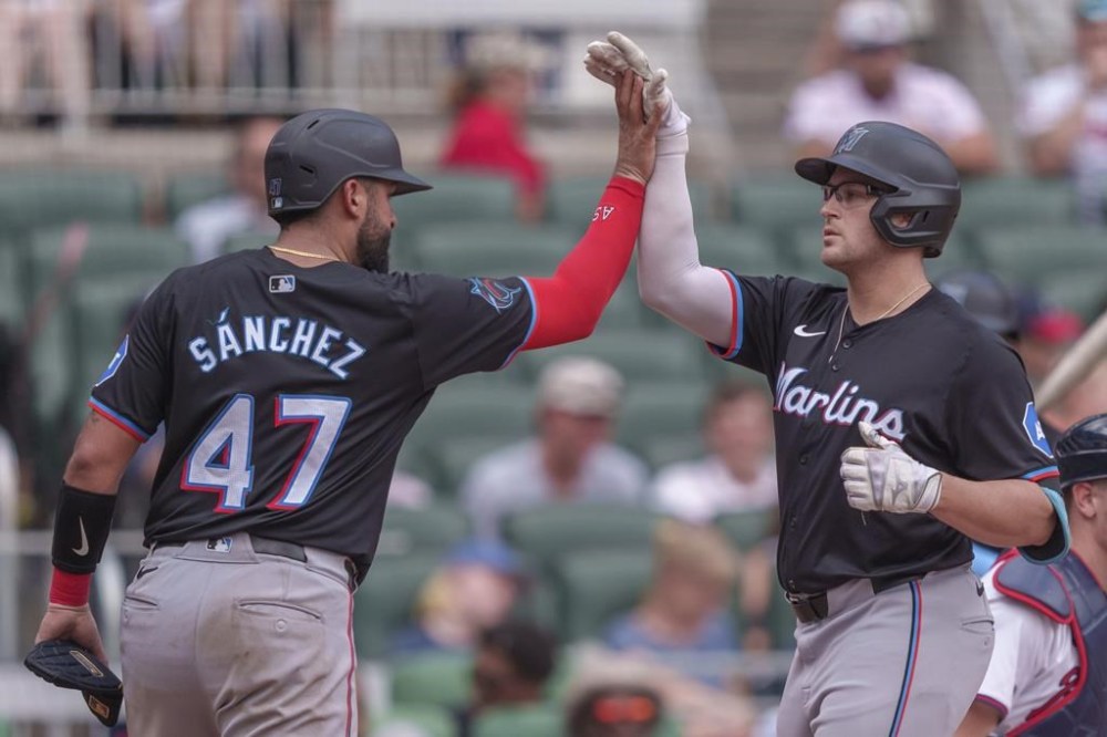 Miami Marlins' Jake Burger, right, high-fives teammate Ali Sánchez, left, as he tags home plate after hitting a three-run home run in the fourth inning of a baseball game against the Atlanta Braves, Sunday, Aug. 4, 2024, in Atlanta. (AP Photo/Jason Allen)