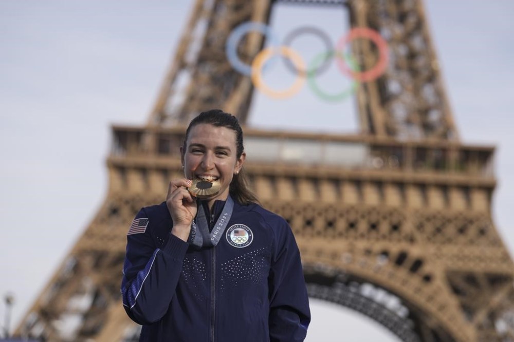 Kristen Faulkner, of the United States, bites the gold medal of the women's road cycling event, at the 2024 Summer Olympics, Sunday, Aug. 4, 2024, in Paris, France. (AP Photo/Thibault Camus)