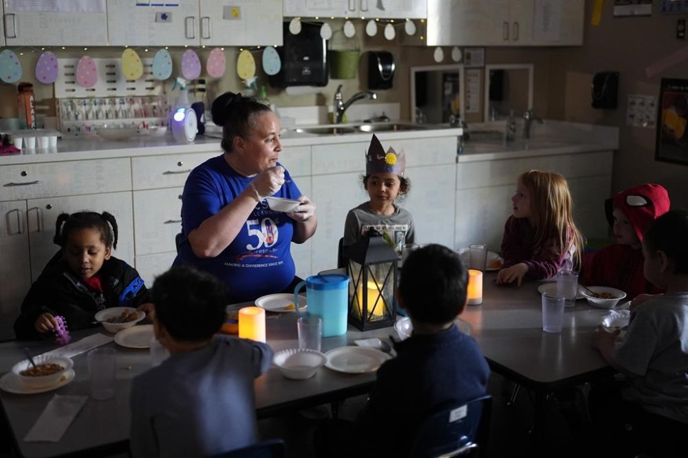 Associate Educator Patty Kramer eats cereal with her students as they have breakfast by electric candlelight at the Meadow Lakes CCS Early Learning, a Head Start center, Tuesday, May 7, 2024, in Wasilla, Alaska. (AP Photo/Lindsey Wasson)