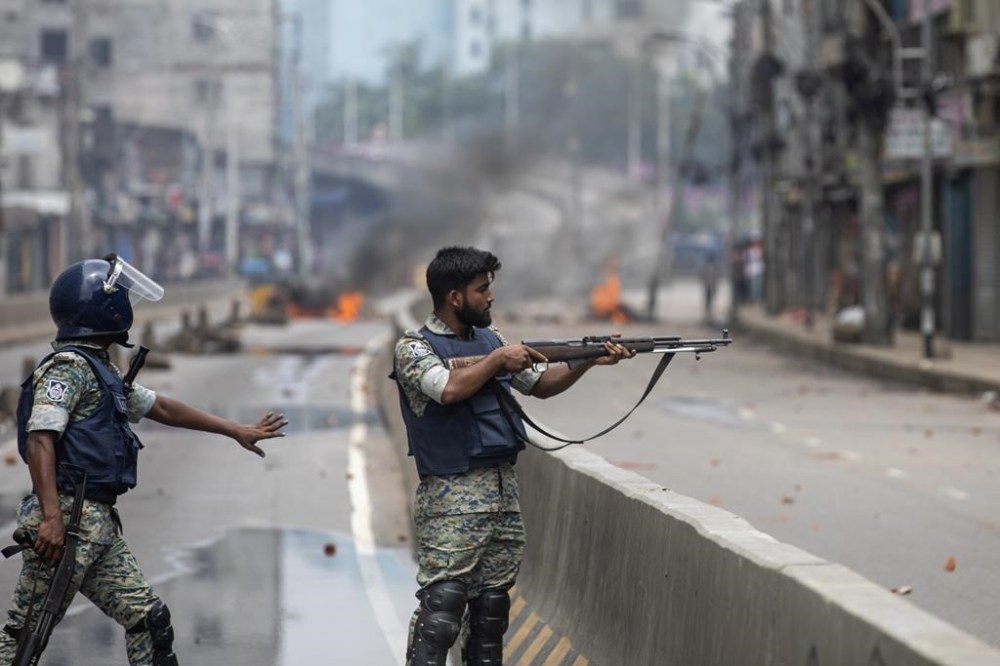 A policeman aims his weapon at protesters during a curfew imposed following violence during protests against Prime Minister Sheikh Hasina and her government, in Dhaka, Bangladesh, Monday, Aug. 5, 2024. (AP Photo/Rajib Dhar)