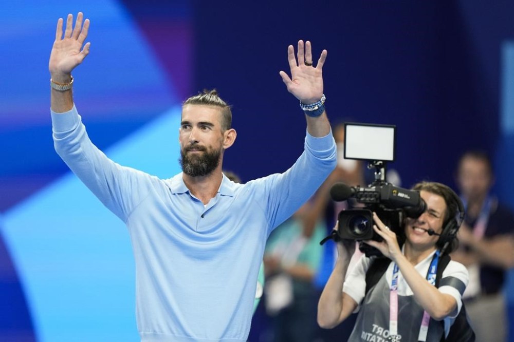 Former Olympic champion Michael Phelps, from the United States, waves to fans ahead of the evening swimming session at the 2024 Summer Olympics, Sunday, July 28, 2024, in Nanterre, France. (AP Photo/Martin Meissner)