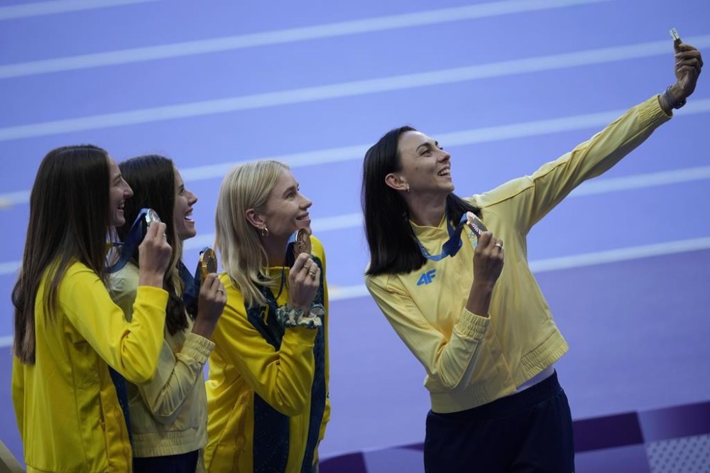 Women's high jump gold medalist Yaroslava Mahuchikh, second left, of Ukraine, silver medalist Nicola Olyslagers, left, of Australia, and dual bronze medal winners Eleanor Patterson, of Australia, and Iryna Gerashchenko, right, of Ukraine, pose for a selfie on the podium at the 2024 Summer Olympics, Monday, Aug. 5, 2024, in Saint-Denis, France. (AP Photo/Martin Meissner)