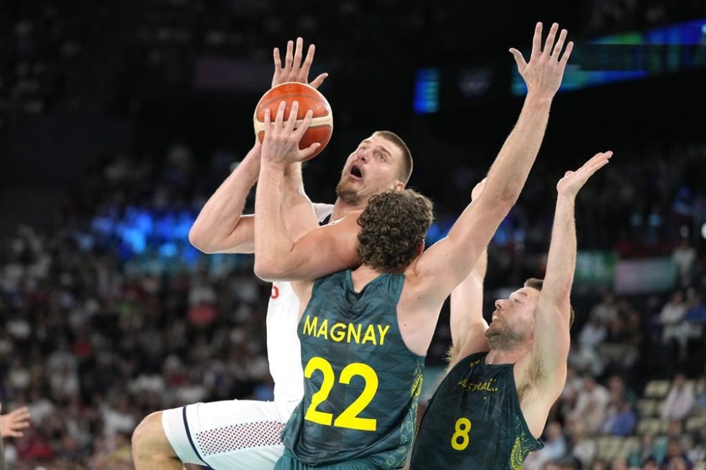 Serbia's Nikola Jokic, left, shoots as Australia'a Will Magnay, center, and Australia'a Matthew Dellavedova defend during a men's quarterfinal game at Bercy Arena at the 2024 Summer Olympics, Tuesday, Aug. 6, 2024, in Paris, France. (AP Photo/Michael Conroy)