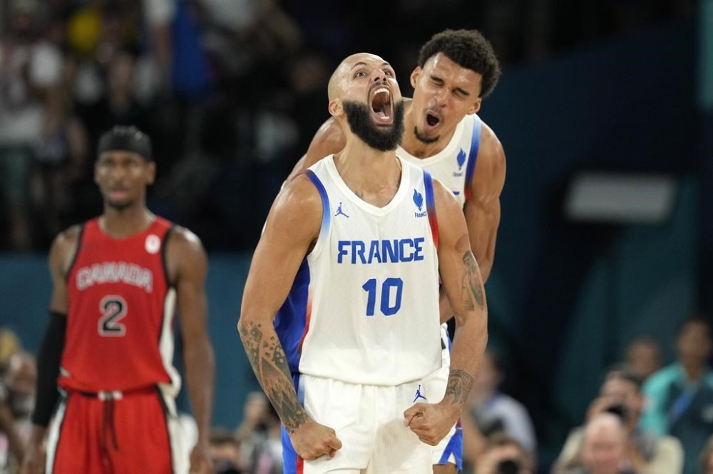 France's Evan Fournier, center, celebrates with France's Victor Wembanyama, right, after scoring as Canada's Shai Gilgeous-Alexander look on during a men's basketball game at the 2024 Summer Olympics, Tuesday, Aug. 6, 2024, in Paris, France. (AP Photo/Michael Conroy)