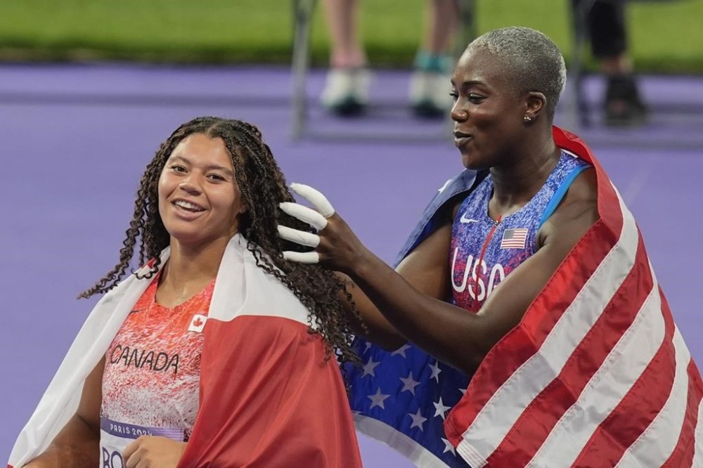 Gold medalist Camryn Rogers, of Canada, gets her hair beautified by silver medalist Annette Nneka Echikunwoke as they celebrate after the women's hammer throw at the 2024 Summer Olympics, Tuesday, Aug. 6, 2024, in Saint-Denis, France. (AP Photo/Rebecca Blackwell)