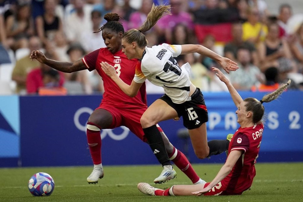 Canada's Gabrielle Carle and Kadeisha Buchanan fight for the ball with Germany's Jule Brand during a women's quarterfinal soccer match between Canada and Germany at the 2024 Summer Olympics, Saturday, Aug. 3, 2024, at Marseille Stadium in Marseille, France. Saturday's Team Canada women's soccer match against Germany has been Canada's most-watched moment of the Paris Olympics to date. (AP Photo/Daniel Cole)