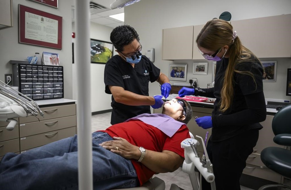 Dr. Melvin Lee, left, performs a tooth extraction for patient Robert McFarlane, who is eligible for the Canadian Dental Care Plan, as team member Sofia Christow-Filleul assists, at his dental clinic in Ottawa, on Wednesday, Aug. 7, 2024. THE CANADIAN PRESS/Justin Tang