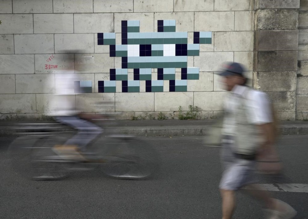 A cyclist rides in front of an Olympic-themed new mosaic by the mysterious French street artist known only by the name Invader, Wednesday Aug. 7, 2024, on the banks of the Seine River, during the 2004 Summer Olympics, in Paris, France. (AP Photo/John Leicester)