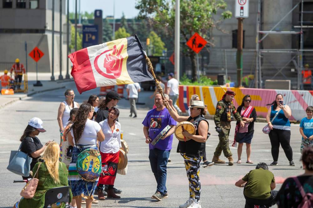 BROOK JONES / FREE PRESS
                                A woman holds an American Indian Movement flag and an aboriginal drum during a round dance at the intersection of Portage Avenue and Main Street Thursday afternoon.