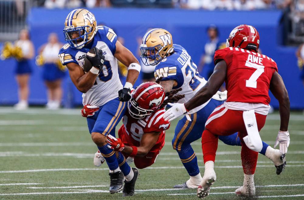Winnipeg Blue Bombers' Nic Demski (10) runs for the first down as Calgary Stampeders' Malcolm Thompson (19) hangs on during first half CFL action in Winnipeg, Friday, July 12, 2024. THE CANADIAN PRESS/John Woods